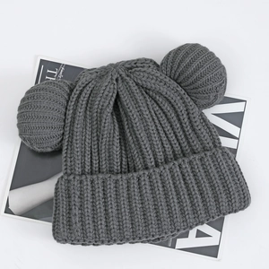 Detailed knit texture and double pom-pom ears of a thick dark grey winter beanie hat