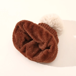 Dettaglio del berretto in maglia marrone con fodera in peluche e pompon bianco morbido