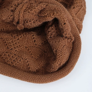 Vista macro della trama a maglia grossa marrone caramello con motivi a treccia del cappello