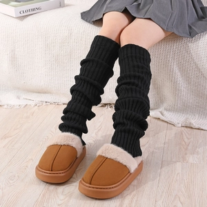 Détail de jambières noires en tricot portées avec des mules à plateforme marron doublées