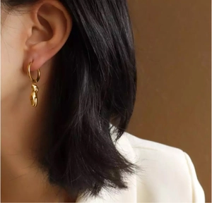 Détail d'une boucle d'oreille dorée 18k avec pendentif corps artistique sur un mannequin