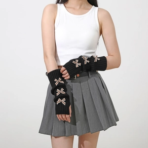 Detail of long black knit arm warmers featuring brown plaid bow accents and thumb holes
