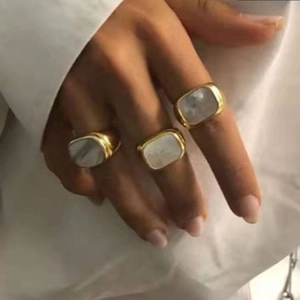 Primer plano de tres anillos de acero dorados 18K con incrustación cuadrada de nácar
