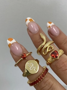 Dettaglio di set anelli placcati oro 18K con zirconi rossi e motivi a cuore e serpente