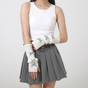 Detail of cream knit arm warmers featuring blue polka dot bow accents and open fingers