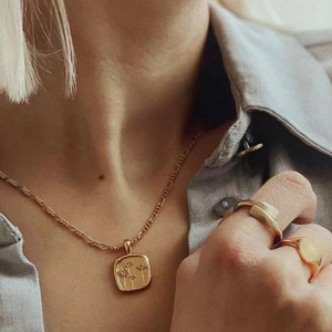 Gouden madeliefje ketting en vintage zegelringen set op een grijze overhemd achtergrond