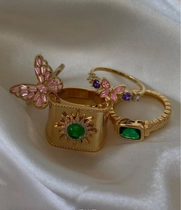 Primer plano de tres anillos vintage bañados en oro de 18k con esmeralda y mariposa