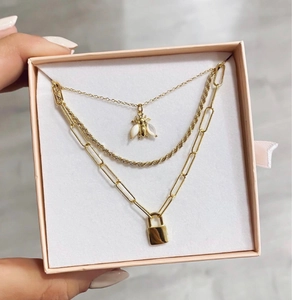 Detail van de 18k gouden dubbele ketting met bij- en slotpendels in een roze geschenkdoos