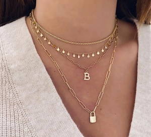 Detail van gelaagde 18k vergulde kettingen met een kristallen letter B en een hangslotje
