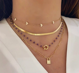 Detail van een gelaagde gouden ketting met halve maan en hangslot hangers op wit