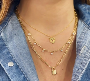 Detail van drielaagse vergulde halsketting met tijgerkop en kleine slot-hangers op denim
