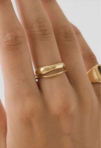 Primer plano de un anillo de onda doble dorado minimalista usado en el dedo acabado brillante