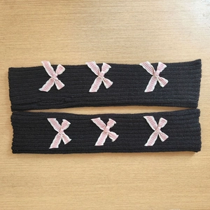 Detail of black knit arm warmers featuring three pink bows and ribbed texture