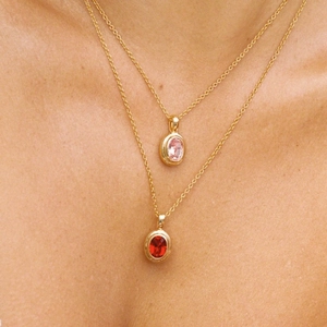 Detail van de dubbellaagse gouden ketting met roze en rode ovale edelsteen hangers