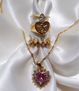 Conjunto de joyas doradas con collar de corazón y anillos de alas de ángel en satén blanco