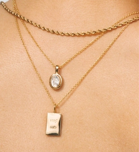 Detail van gelaagde gouden ketting met zirkoon hanger en gegraveerde bedel