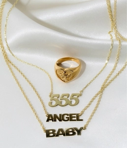 Anillo de corazón con alas de ángel dorado y collares sobre fondo de seda blanca