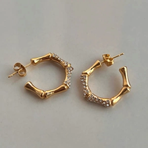 Detalle de pendientes tipo C de bambú en oro 18K con circonitas sobre fondo gris
