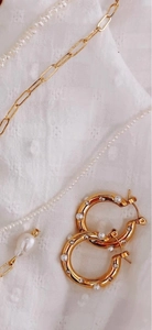 Détail de boucles d'oreilles créoles dorées avec perles et cristaux sur tissu blanc