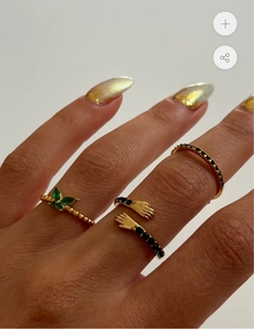 Dettaglio di anelli placcati oro 18K con design a mani che abbracciano e pietre verdi