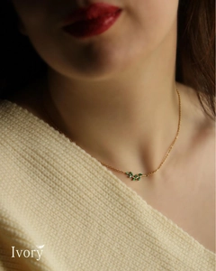 Detail van vergulde ketting met groene edelsteen bladeren op een beige gebreide achtergrond
