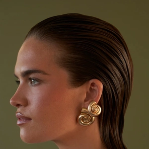 Orecchini a spirale in acciaio al titanio placcati oro 18K indossati da modella su verde