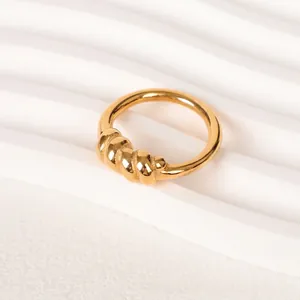 Eleganter goldener Ring mit gedrehten Metallperlen auf modernem weißem Ständer