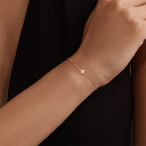 Détail d'un bracelet doré avec pendentif étoile et perle centrale porté au poignet d'un mannequin