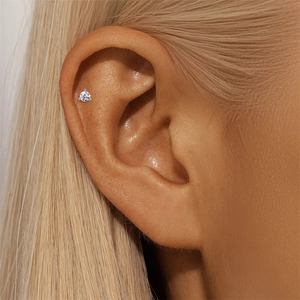 Macro view of a tiny moissanite stud earring worn on the cartilage with silver metal finish