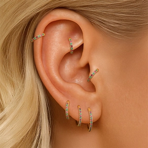 Close-up of gold hoop earrings with pavé pink and green stones on a model ear