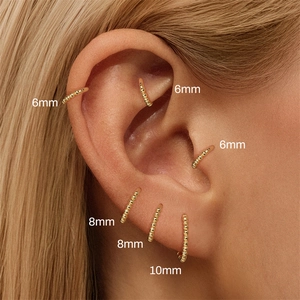 Nahaufnahme von 6mm, 8mm und 10mm goldene Kugelohrringe an verschiedenen Piercingstellen