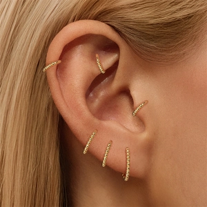 Makro-Detail von goldenen Perlen-Ohrringen mit mehreren Knorpel-Piercings am Ohr gezeigt