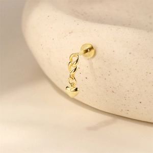 Detailopname van een gouden oorknopje met een gedraaide ketting en een hartvormige hanger
