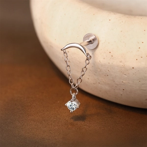 Detail of s925 silver crescent moon earring with hanging moissanite chain on a ceramic edge