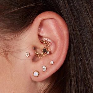Détail du piercing d'oreille couronne dorée avec clous d'opale et pierres de zircone