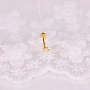 Macro detail of a golden curved barbell piercing with a white zircon on lace background