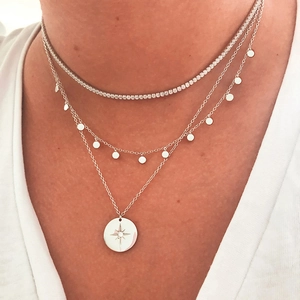 Macro shot of layered S925 silver tennis chain and starburst medallion necklaces