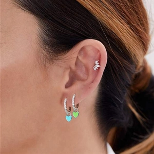 Model wearing CZ paved brass hoop earrings with blue and green heart enamel charms