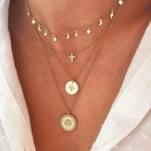 Close-up of layered gold necklaces with star, moon, cross and coin pendants on model