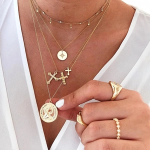 Detail of layered gold necklaces with octagonal star, cross, and Elizabeth coin pendants