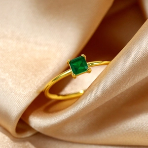 Macro view of square emerald stone set on a polished gold band over champagne silk
