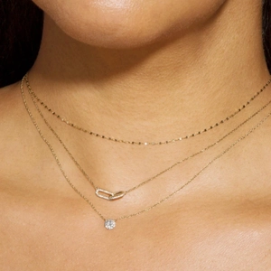Dettaglio delle collane a tre strati in oro con pendenti geometrici in pavé di zirconi