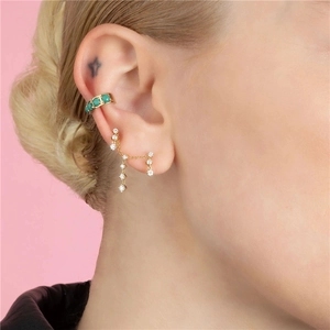 Detalle de ear cuff dorado con piedras verdes y pendiente de cadena de circonita colgante