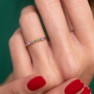 Close-up of gold geometric ring with purple and green crystals on a finger