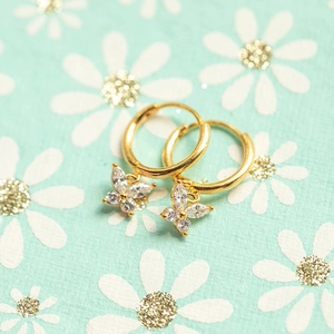 Detailed close-up of golden butterfly earrings with marquise-cut zircon stones on green floral background