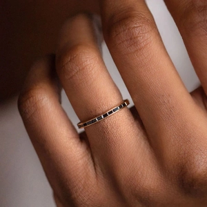 Macro detail of slim rose gold ring set with a row of rectangular black gemstones
