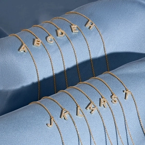 Macro detail of gold-plated S925 silver initial necklaces with cubic zirconia on blue silk
