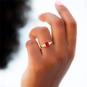 Close-up of a gold ring with rectangular red gemstone and side baguette diamonds