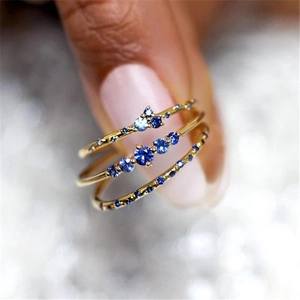 Detail of three stacked gold rings with blue gemstones on a hand with sparkling background