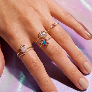 Close-up of stacked gold rings with opal heart and colorful gemstones on purple silk
